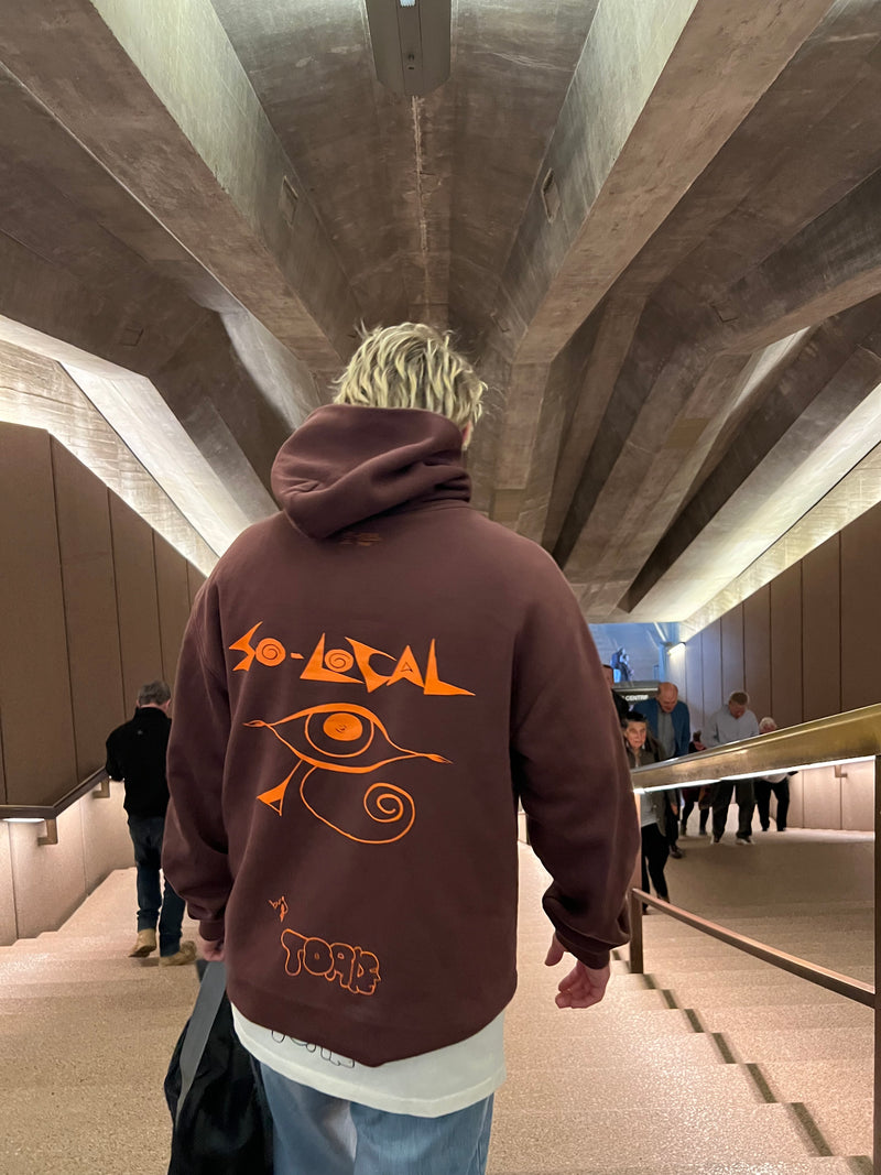 "I SEE YOU" SO LOCAL brown hoodie, lifestyle shot walking through Sydney Opera House concourse